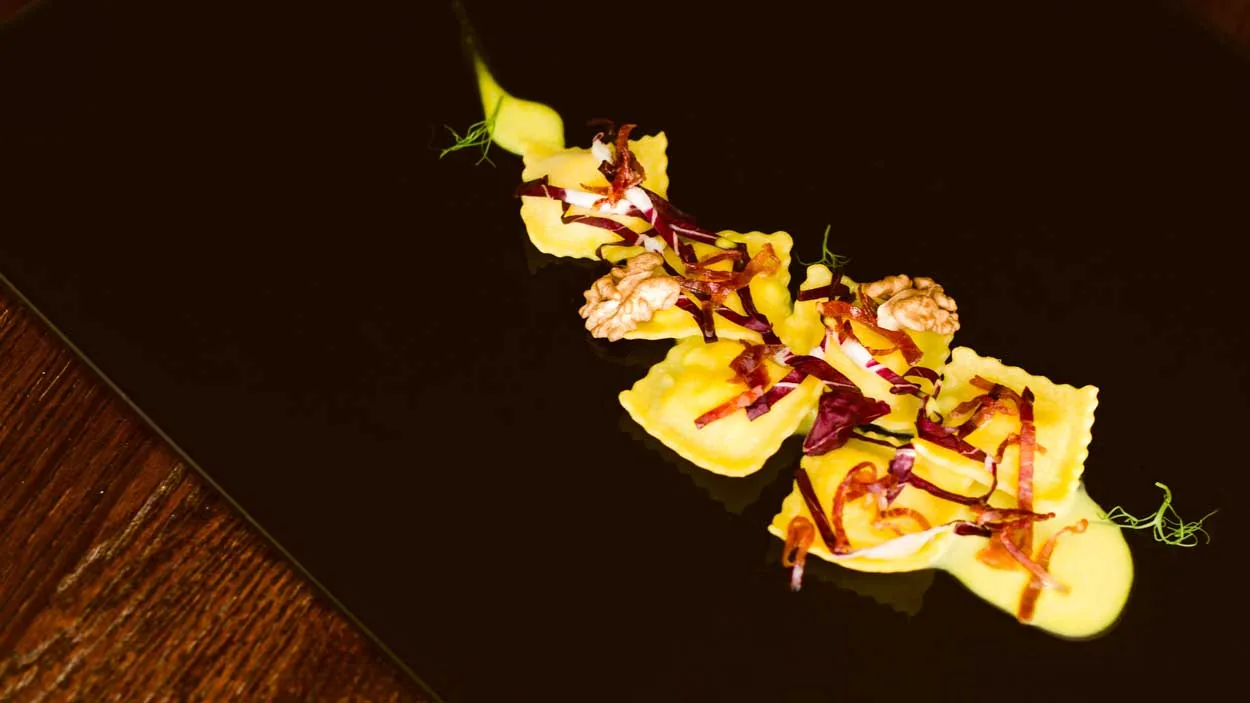 Ravioli con radicchio, guanciale e noci su piatto nero